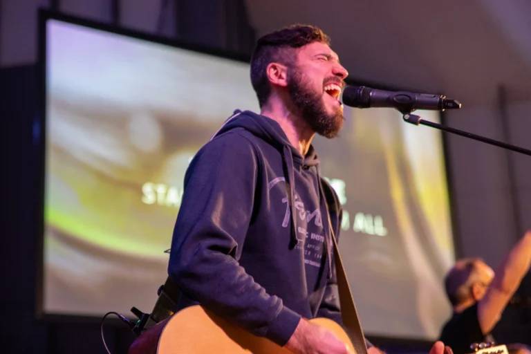 A worship leader singing and playing guitar leading people in worship