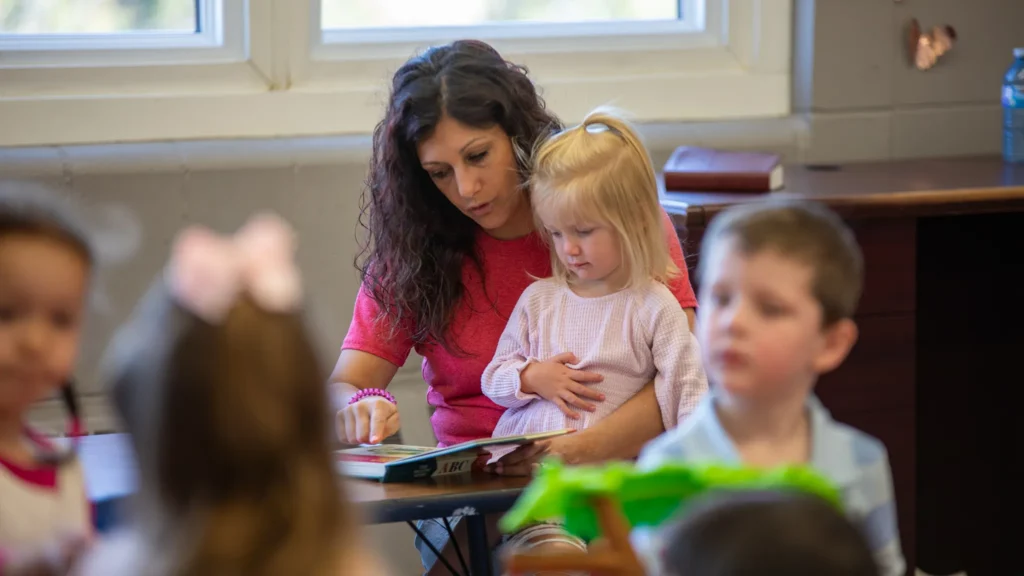 A sunday school teacher with a child on her lap reading a book